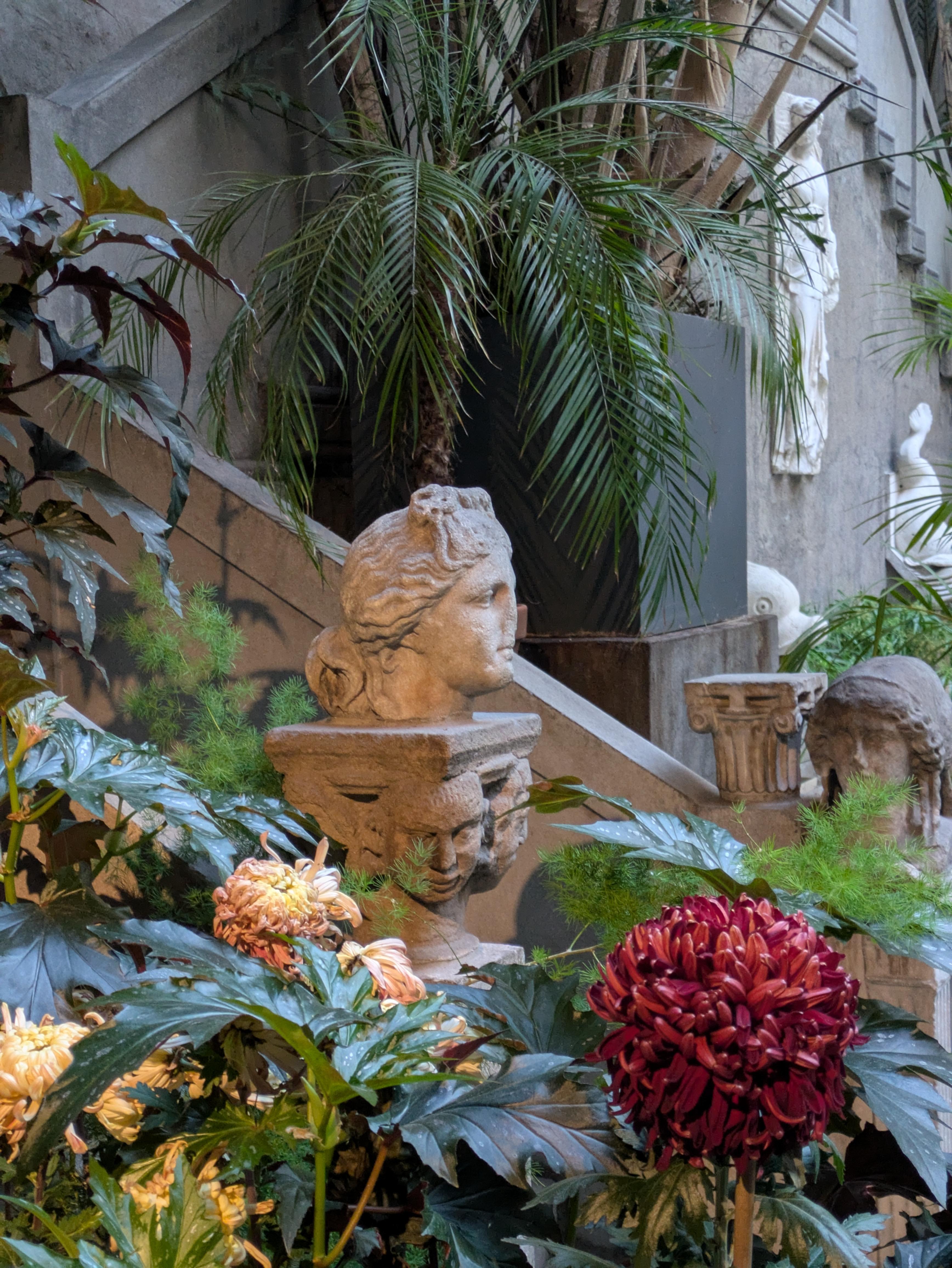 An ancient roman bust stands among flowers and greenery.