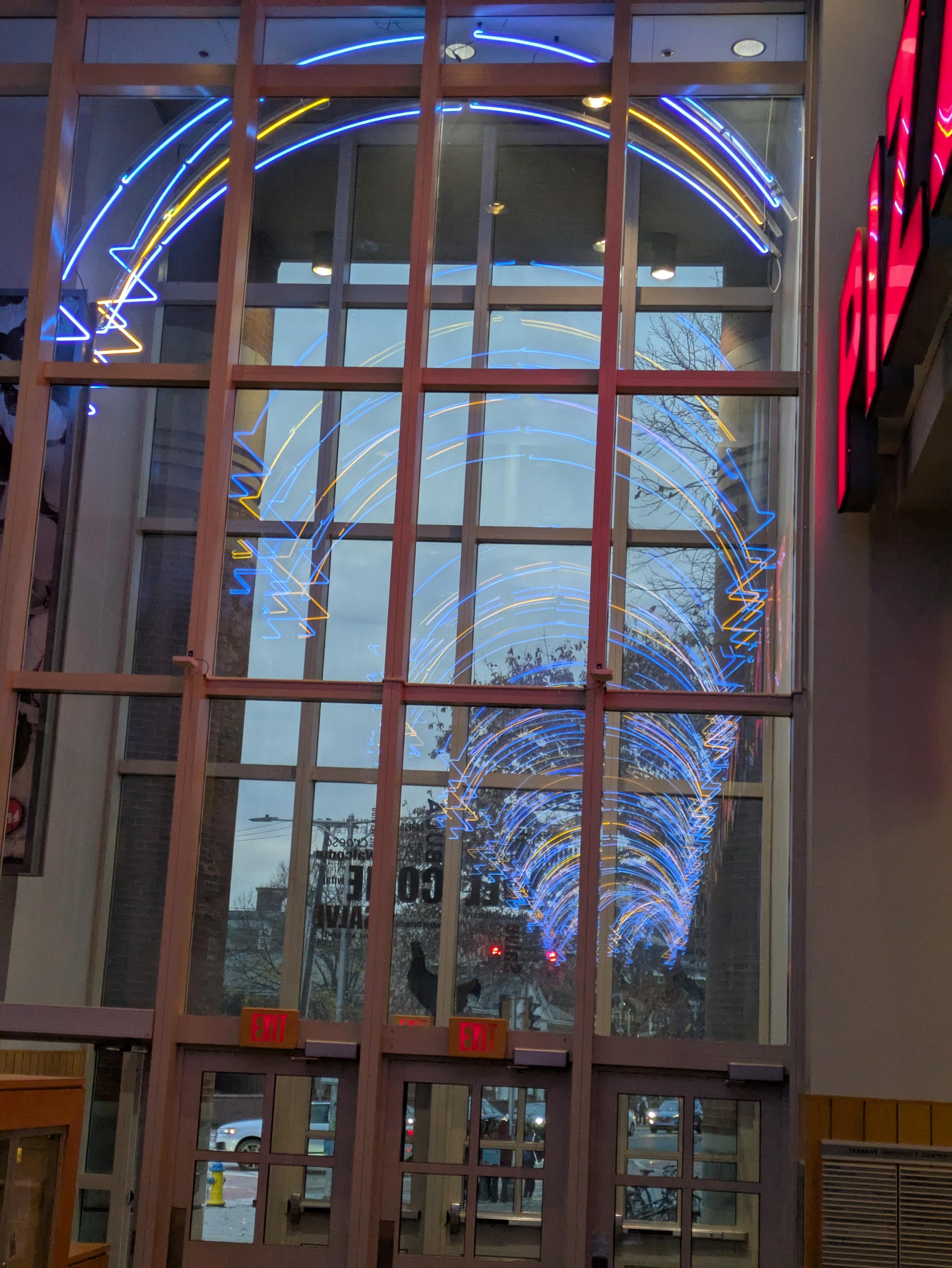 A picture of the exit of a building. It is dusk, and the blue and yellow lights reflect infinitely in the window.